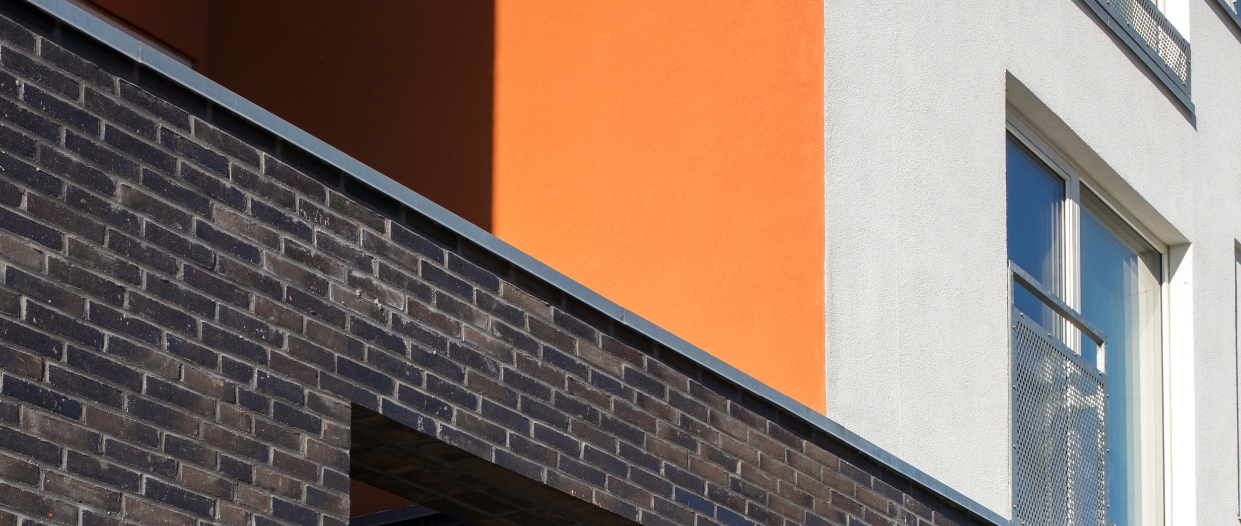 Basen er udført med mørkbrændte teglsten som en reference til havnens lavere huse, mens de øvrige facader fremstår med pudsede flader i hvid og en varm orange farve.